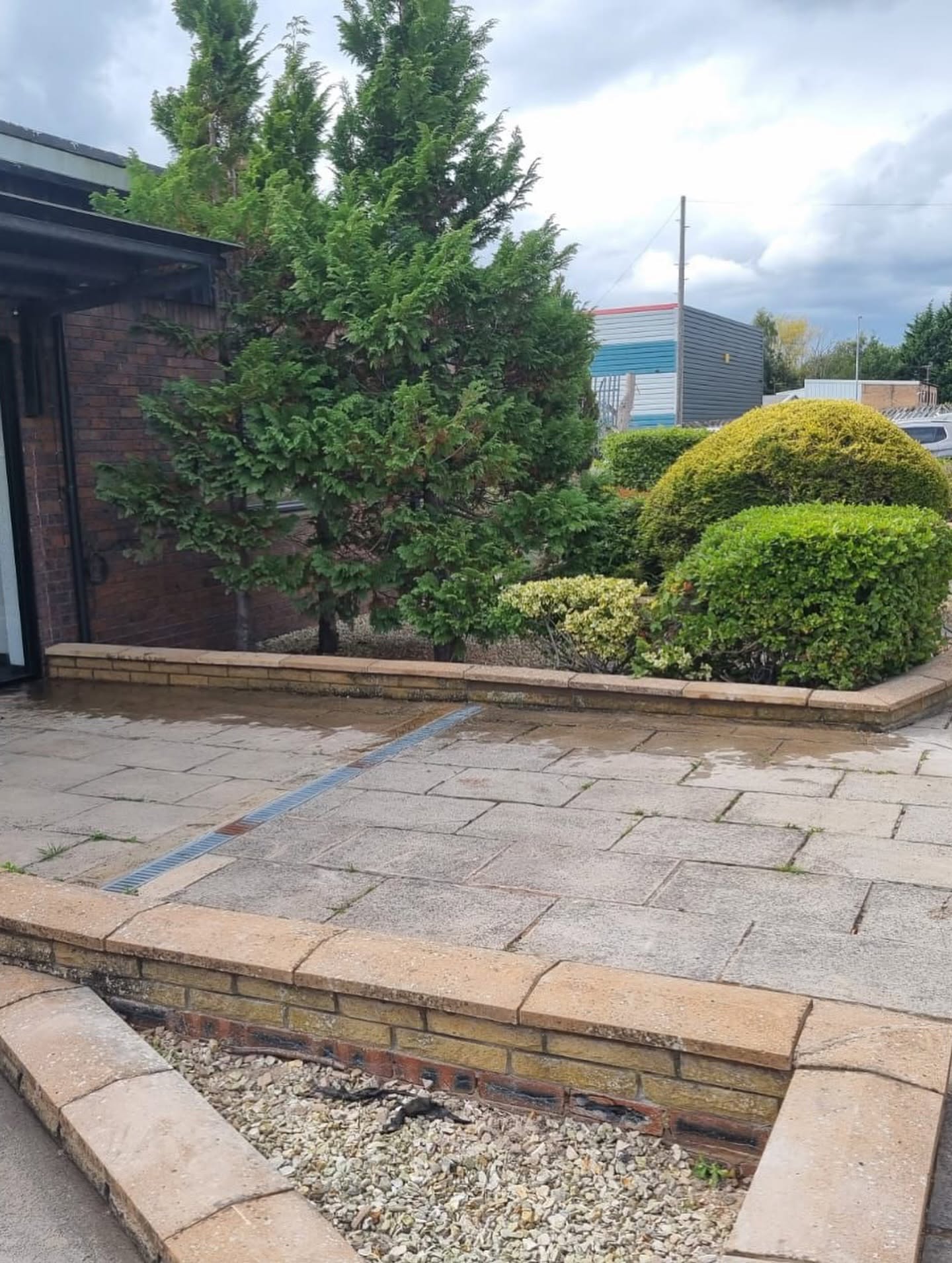 Paved patio and low brick walls bordering well-kept shrubs